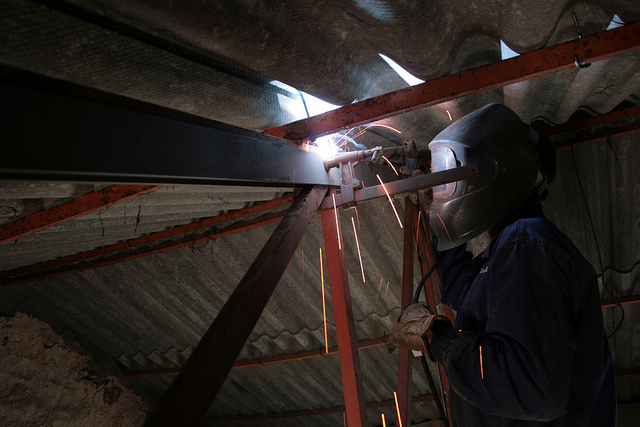 Foto de un operario realizando una soldadura en una cercha de un tejado.
